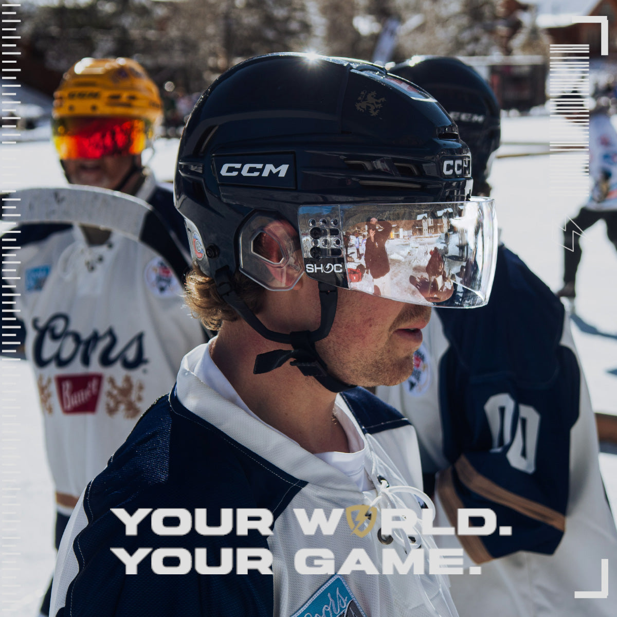 Person wearing a hockey helmet with a Clear Mirror SHOC Hockey Visor visible brand logo, surrounded by other hockey players on a snowy field.