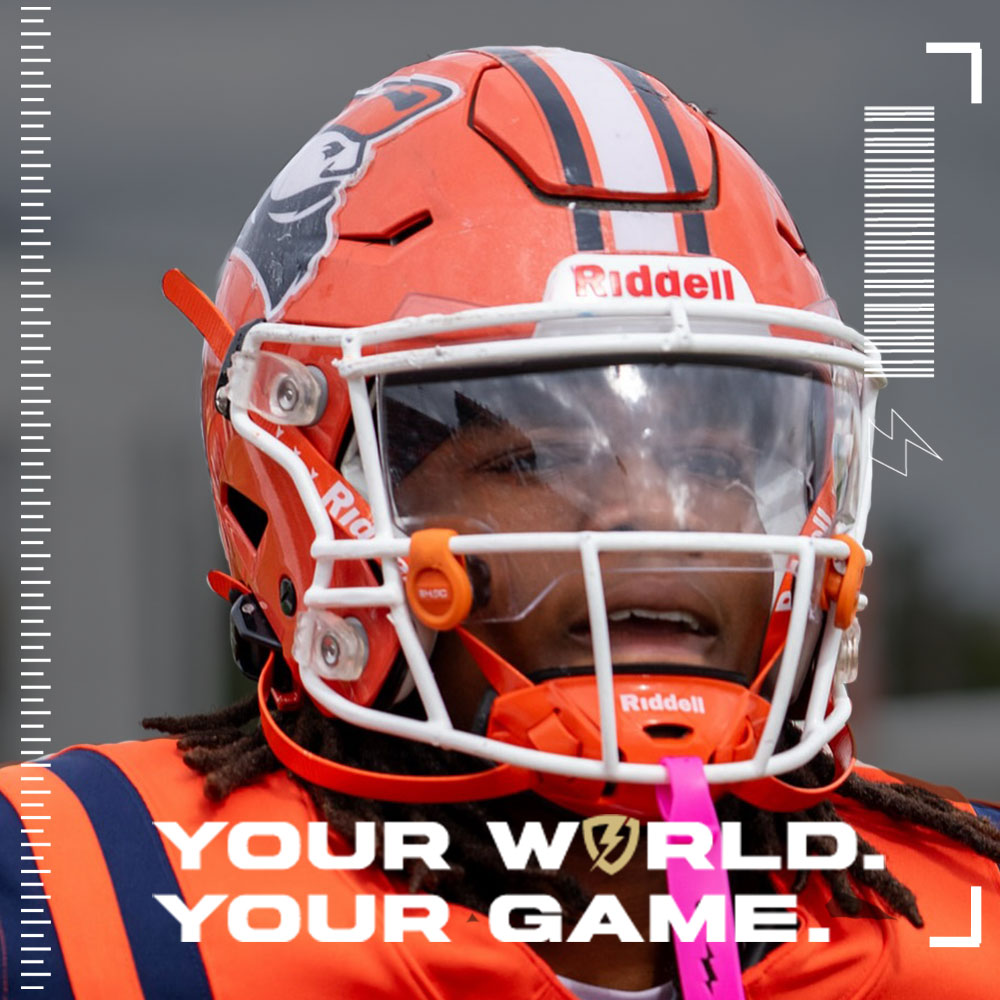 Person wearing an orange football helmet and uniform with a clear SHOC Visor and 'Riddell' branding, text 'Your World. Your Game.'